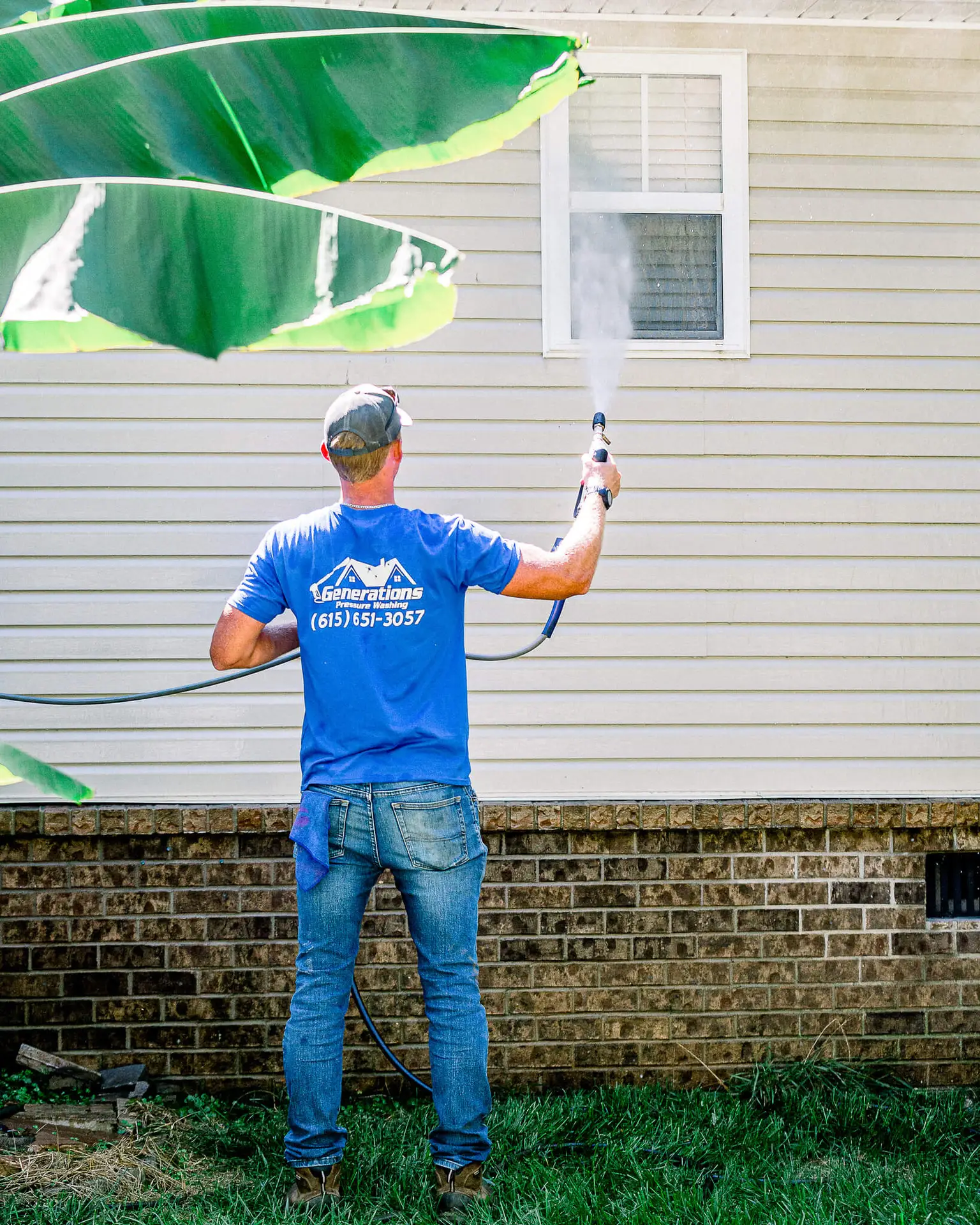 A professional technician using a water-fed pole brush system to clean a second-story grid window on a residential home.